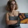 Person in a checkered dress presenting a small female nude painting in warm shades of brown and orange