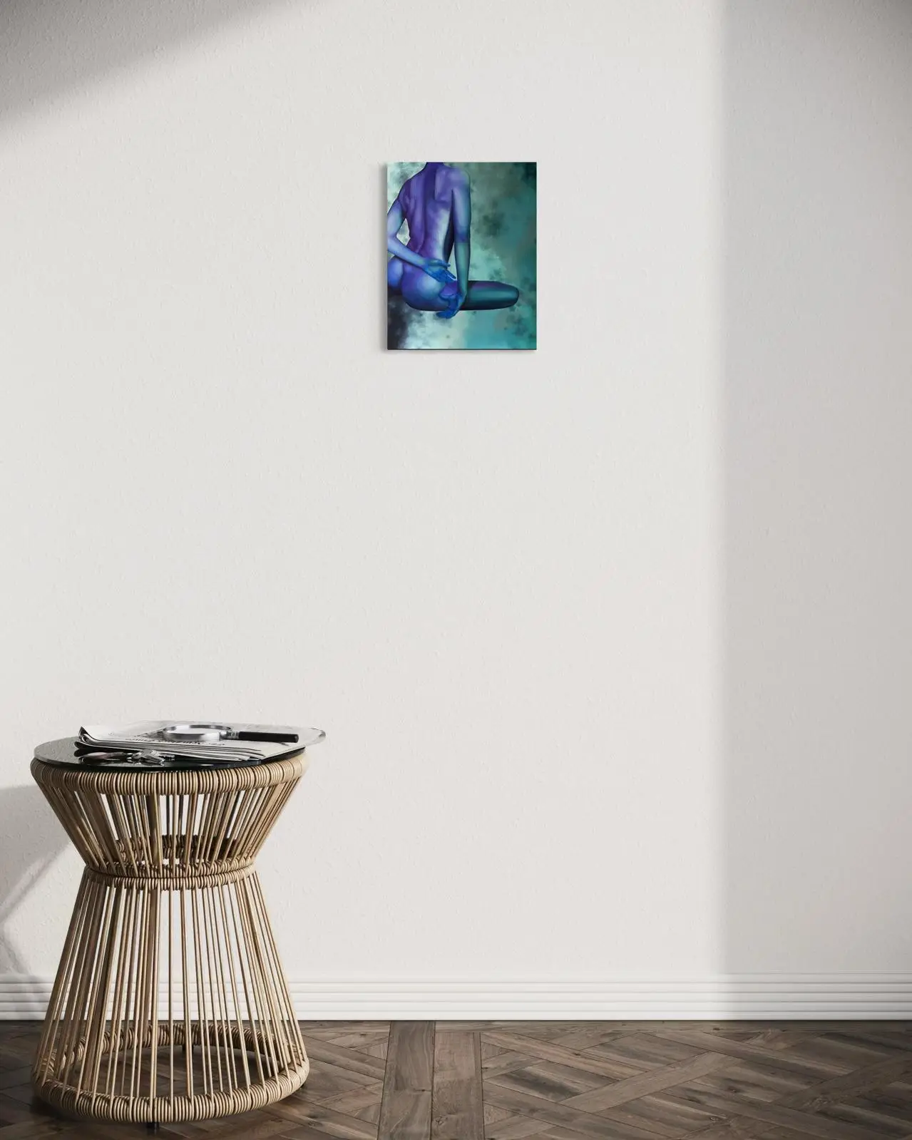 Modern, bright interior with a wicker side table and a painting of a female nude in cool blue and turquoise tones hanging on a white wall