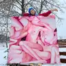 A person standing behind a large painting with pink female nudes, holding it on snow-covered stairs
