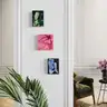 Three colorful paintings of female bodies on a white wall in a stylish interior with a plant and armchair