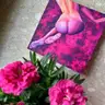 Small painting of a female silhouette on a pink background, photographed on a windowsill next to pink flowers