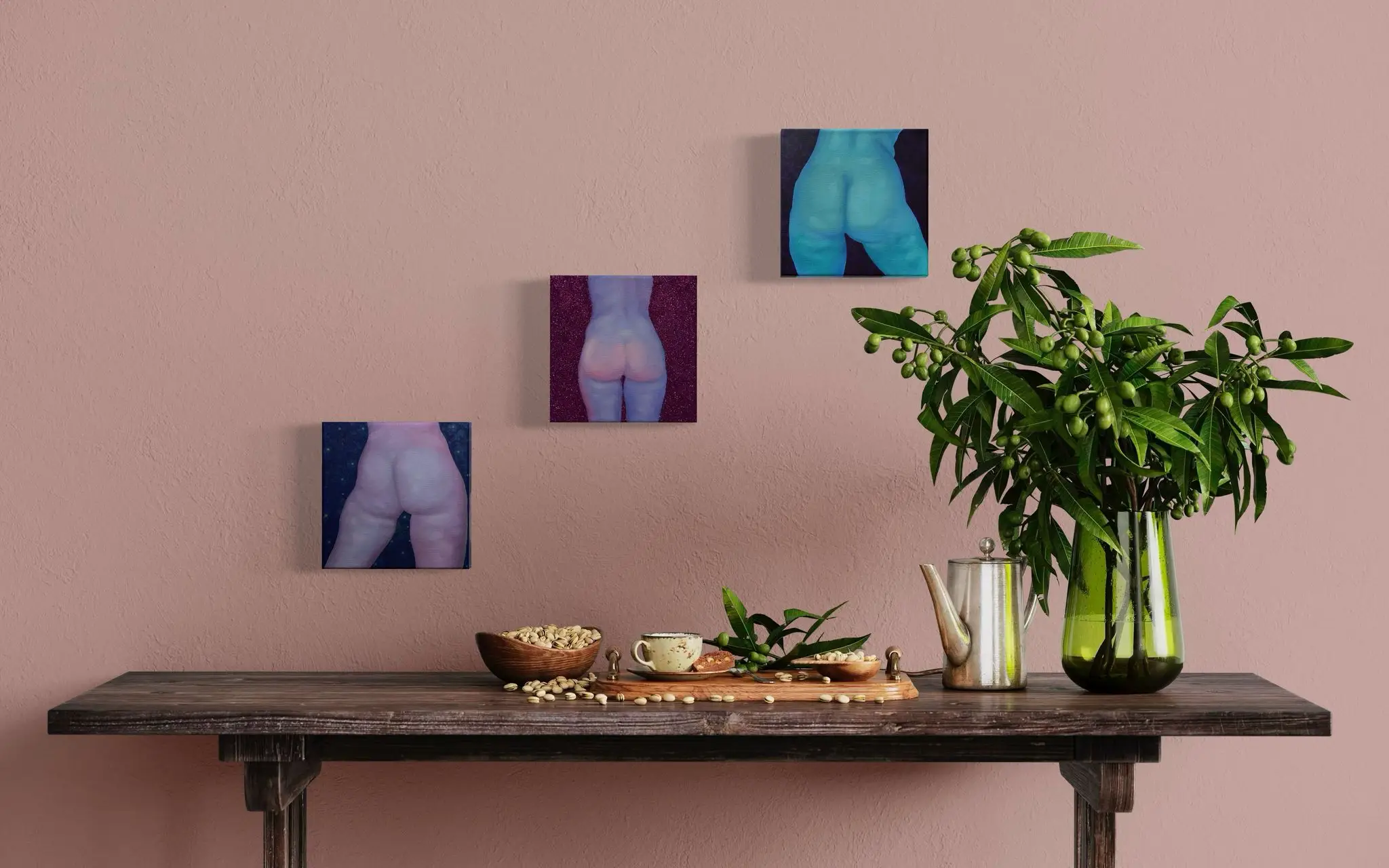 Zestaw trzech obrazów z aktami kobiecymi w chłodnych tonach na różowej ścianie nad drewnianym stołem