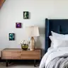 Three colorful female nude artworks hanging above a wooden nightstand and lamp in a bedroom