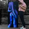 Person in a pink sweatshirt presenting a large painting of a female nude in shades of blue and purple, in a natural setting