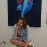 Artist sitting on a stool in front of a large painting of a female nude in shades of blue and pink